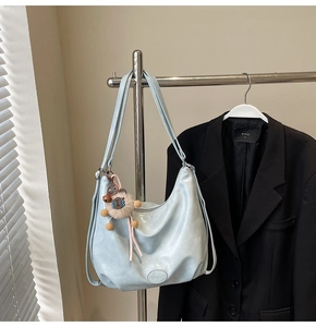 Dettaglio borsa hobo in PU celeste lucido con pieghe e ciondolo orsetto marrone