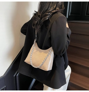 Detail der beigefarbenen gesteppten Baguette-Tasche mit Silberkette an einem Model im Anzug