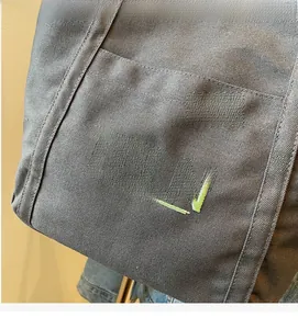 Close-up of gray canvas tote bag featuring green TELN embroidery and side pocket detail