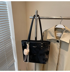 Detail of black tote bag with marble pattern, golden logo, and plush bear charm
