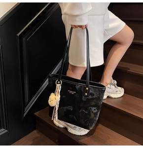 Classic black tote bag with floral texture and cute bear pendant on a wooden staircase
