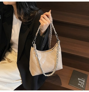 Detailansicht beige gesteppte Hobo-Tasche mit dicker Silberkette auf dunklen Holzstufen