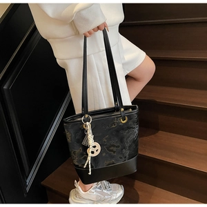 Dettaglio della borsa tote nera con motivo a rilievo e ciondolo beige segno della pace