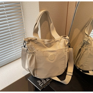 Detail view of cream nylon tote bag featuring drawstring side pockets and wide strap