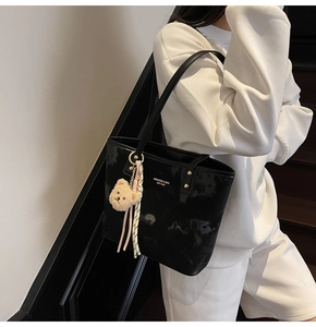 Detail of glossy black patent leather bucket bag with gold lettering and bear charm