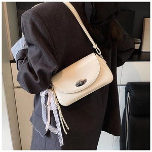 Détail du sac baguette en similicuir blanc cassé avec boucle argentée et breloque en dentelle
