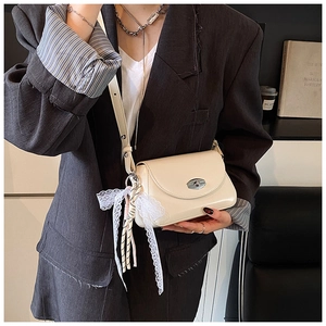 Gros plan sur un sac en cuir blanc cassé avec pendentif en dentelle et fermoir rotatif