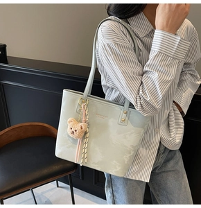 Side view of a mint green tote bag with cloud patterns and a plush bear pendant charm