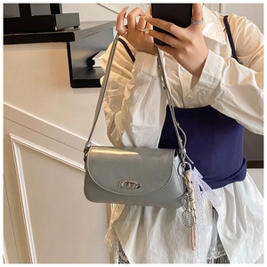Détail d'un sac à bandoulière bleu clair avec boucle argentée et charm en dentelle