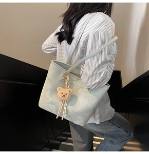 Detail of light blue bucket bag with faux leather texture and brown plush bear charm