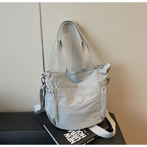 Detail view of a light gray nylon tote bag featuring a side elastic pocket and a round logo