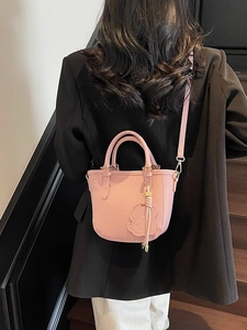 Pink lychee grain leather bucket bag with cute rabbit charm held by model on stairs