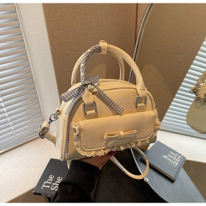 Detail van crème PU-leren tas met kanten rand, strik en geruit lint rond het handvat