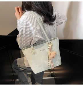 Detail of light blue tote bag with fuzzy bear charm and branded text on a staircase