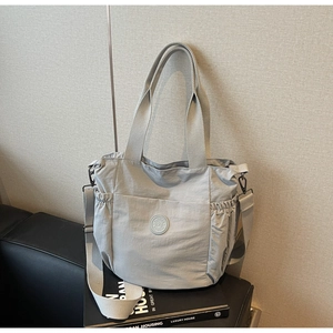 Detail of grey nylon tote bag with fashion logo and side drawstring on a black sofa