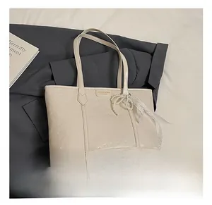 Detail of cream tote bag with heart embossing, pearl bow and lace charm accessory