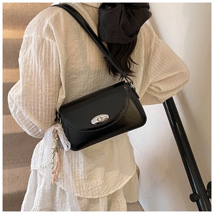 Détail d'un sac d'épaule noir brillant avec fermoir argenté et foulard décoratif en soie
