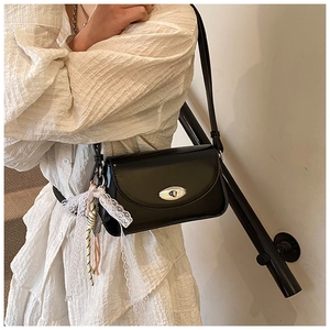 Détail du sac bandoulière noir brillant avec boucle argentée et nœud en dentelle blanche