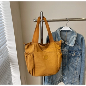 Detail of a ginger yellow nylon tote bag with side pockets and a round logo on the front