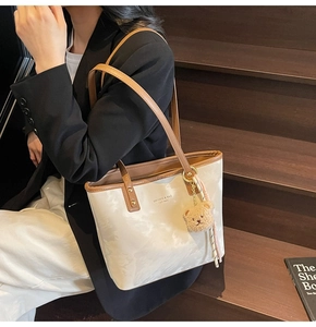 Detail of a marble-patterned tote bag in off-white with a plush bear charm on wooden steps