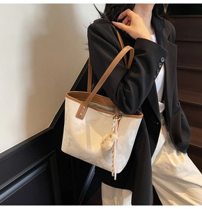 Detail of cream bucket bag with brown handles and a cute plush bear charm on strap