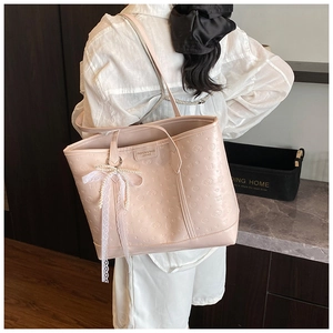 Close-up of pink tote bag with embossed pattern, lace bow, and pearly charm detail