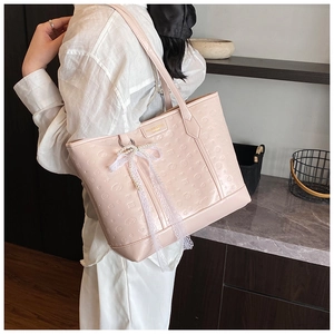Detail of light pink tote bag with embossed face patterns and pearl bow charm accessory