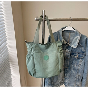 Detail view of sage green tote bag with large front pocket and drawstring side pouches