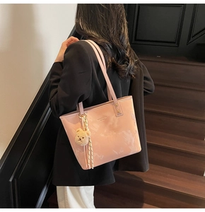 Pink glossy tote bag with teddy bear charm shown on a model against stairs