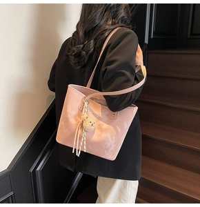 Close-up of pink patent leather bucket bag with plush bear charm and thin shoulder strap