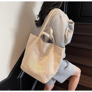 Detail of green TELN embroidery on beige canvas tote bag with thick shoulder strap