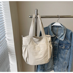 Detail of off-white nylon tote bag with drawstring side pockets and embossed logo