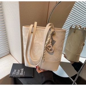 Dettaglio della borsa tote beige goffrata con motivi a cartoni e ciondolo decorativo in corda