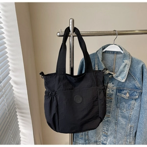 Detail of a black large-capacity canvas tote bag with side pockets on a stainless hanger