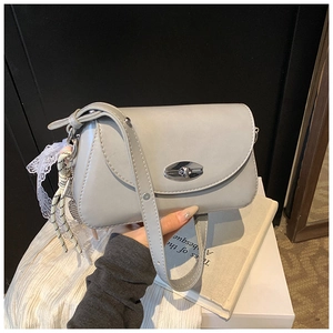 Détail du sac bandoulière gris clair avec fermoir rotatif argenté et breloque en dentelle