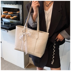 Close-up of cream tote bag featuring embossed cartoon patterns and a pearl lace bow charm