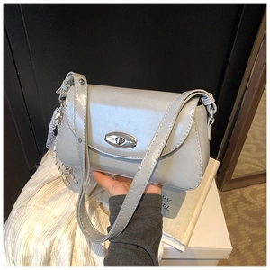 Détail du sac à bandoulière argenté avec fermoir rotatif et pendentif tissé élégant