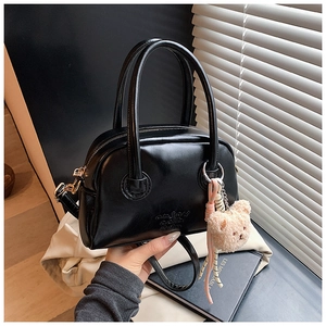 Détail du sac Boston en cuir ciré noir avec texte embossé et breloque d'ours en peluche