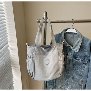 Detail of grey canvas tote bag featuring a round logo badge and drawstring side pockets
