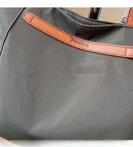 Detail of durable grey oxford fabric and embossed leather logo strap on a large tote bag