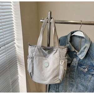 Close-up of light gray nylon tote bag with drawstring side pockets and logo patch