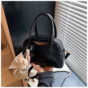 Détail du sac Boston noir avec gaufrage, breloque ours en peluche et fermeture dorée