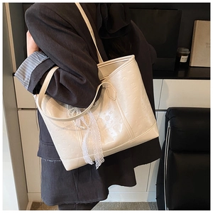 Detail of white large tote bag featuring embossed patterns and pearl lace bow accessory