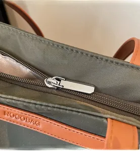 Macro shot of silver metal zipper and brown leather trim on olive oxford tote bag