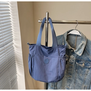 Detail of dark blue nylon tote bag with side elastic pockets and round silicone logo