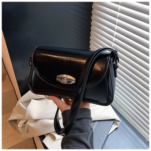 Détail d'un sac à bandoulière noir brillant avec un fermoir rotatif ovale en métal argenté