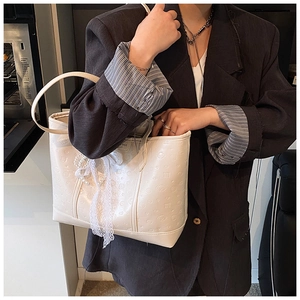 Detail of white tote bag featuring embossed cartoon patterns and a delicate lace bow
