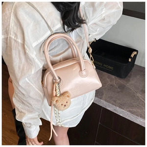 Détail du sac Boston en cuir rose avec texte embossé et breloque ours en peluche doux