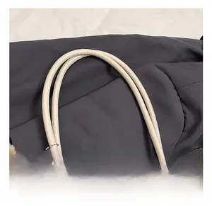 Macro shot of a cream leather tote bag featuring cylindrical handles and a brown plush charm