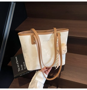 Detail view of contrast tote bag with marble texture and plush bear charm on wooden steps